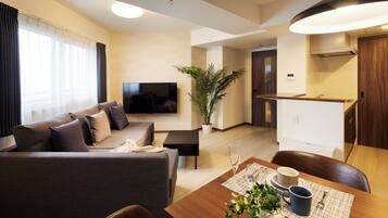 A modern living room with a sofa, a TV, a dining table with chairs, and a kitchen area.