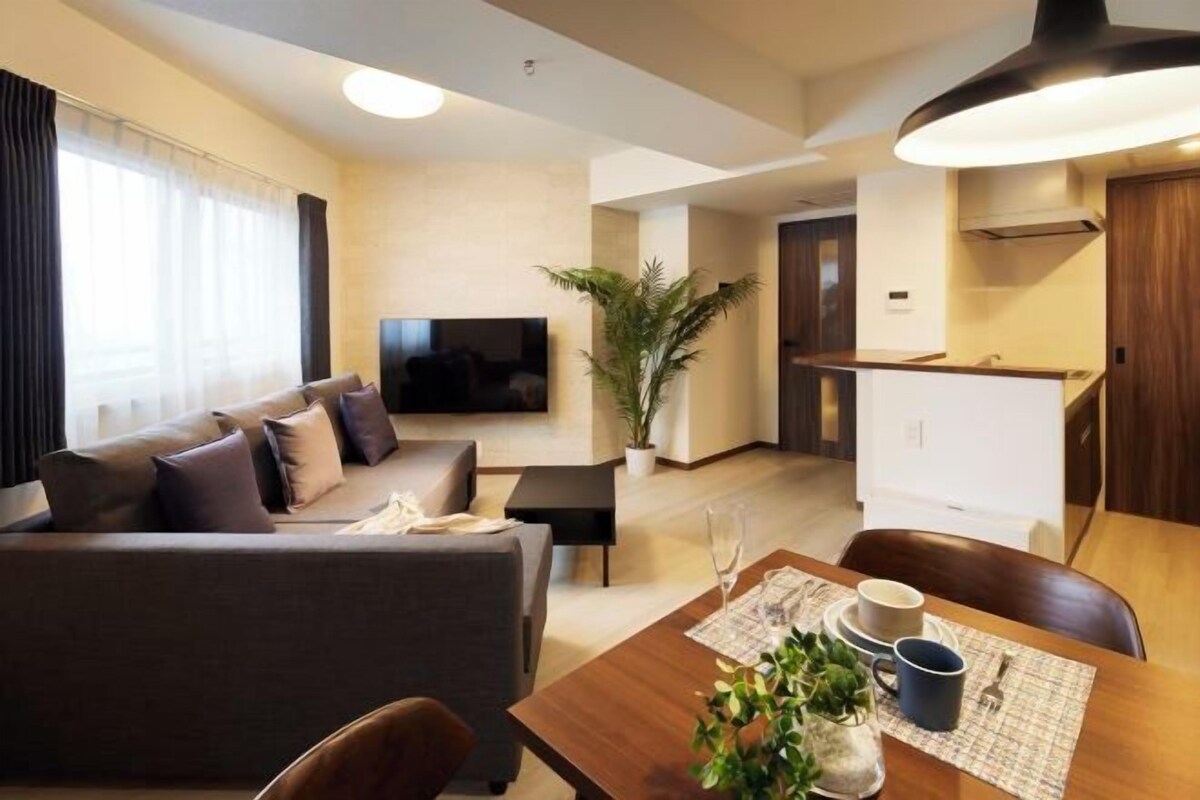 A modern living room with a sofa, a dining table with chairs, a TV, and a kitchen area.