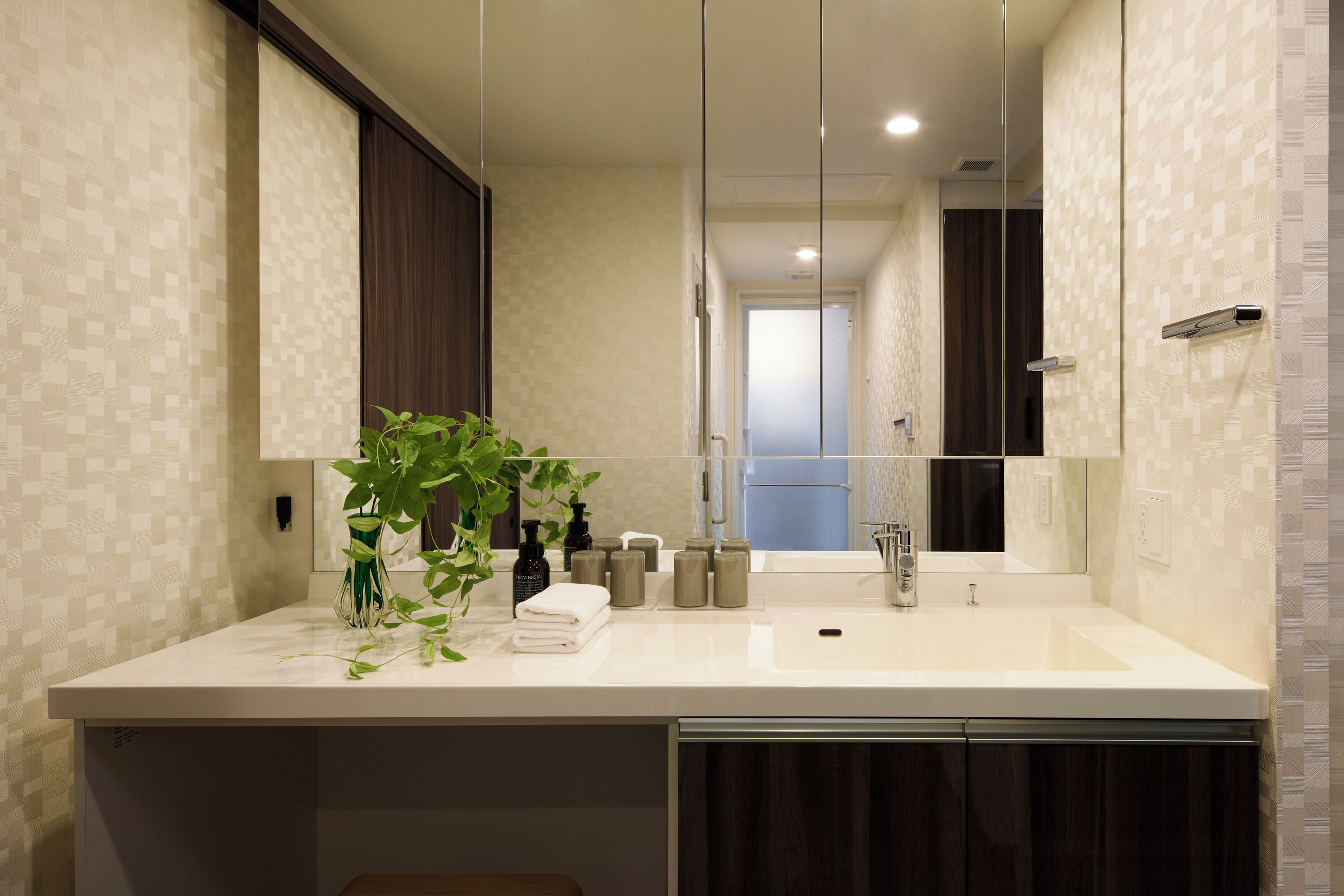Un baño moderno con un espejo grande, encimera blanca y una planta en maceta.