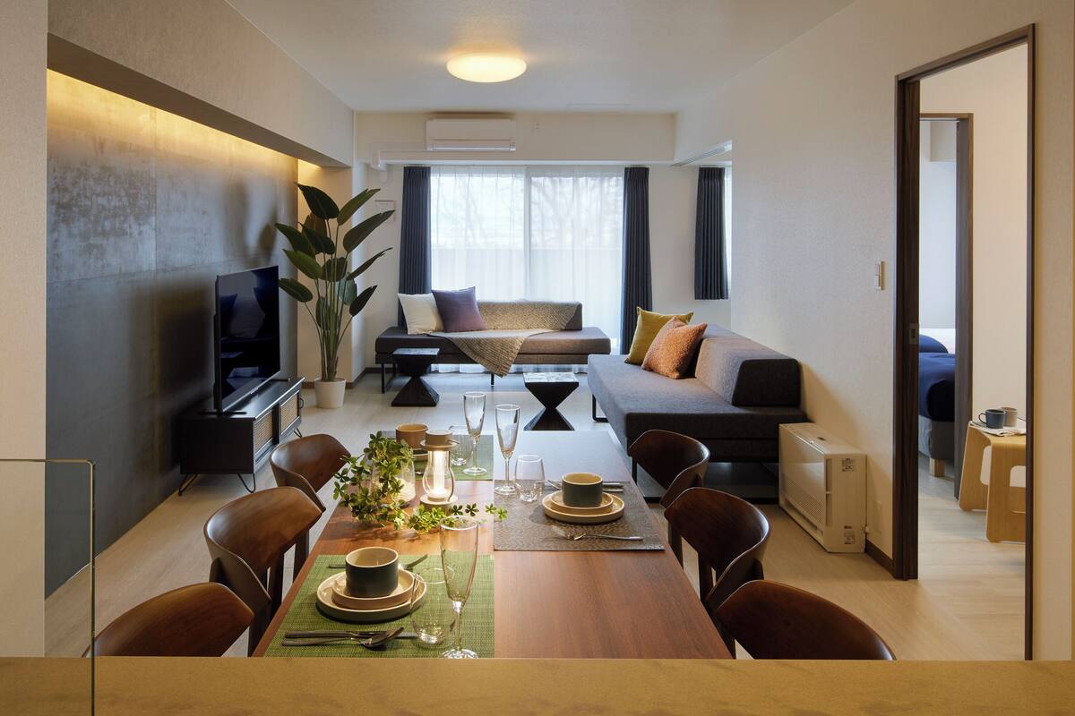 A modern living room with a sofa, dining table set for four, and a television on a stand.