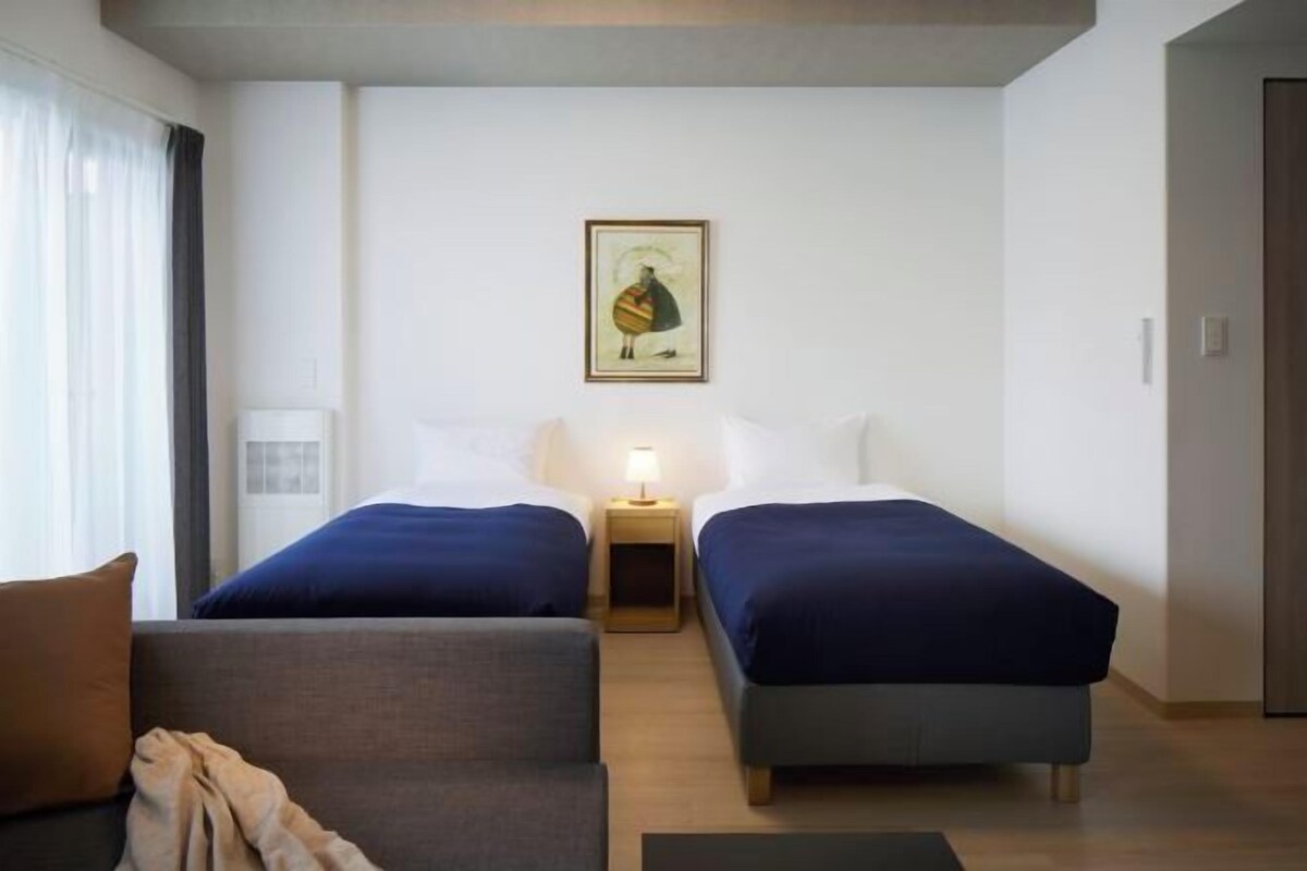 Una habitación de hotel con dos camas individuales, un sofá, una lámpara y un cuadro en la pared.