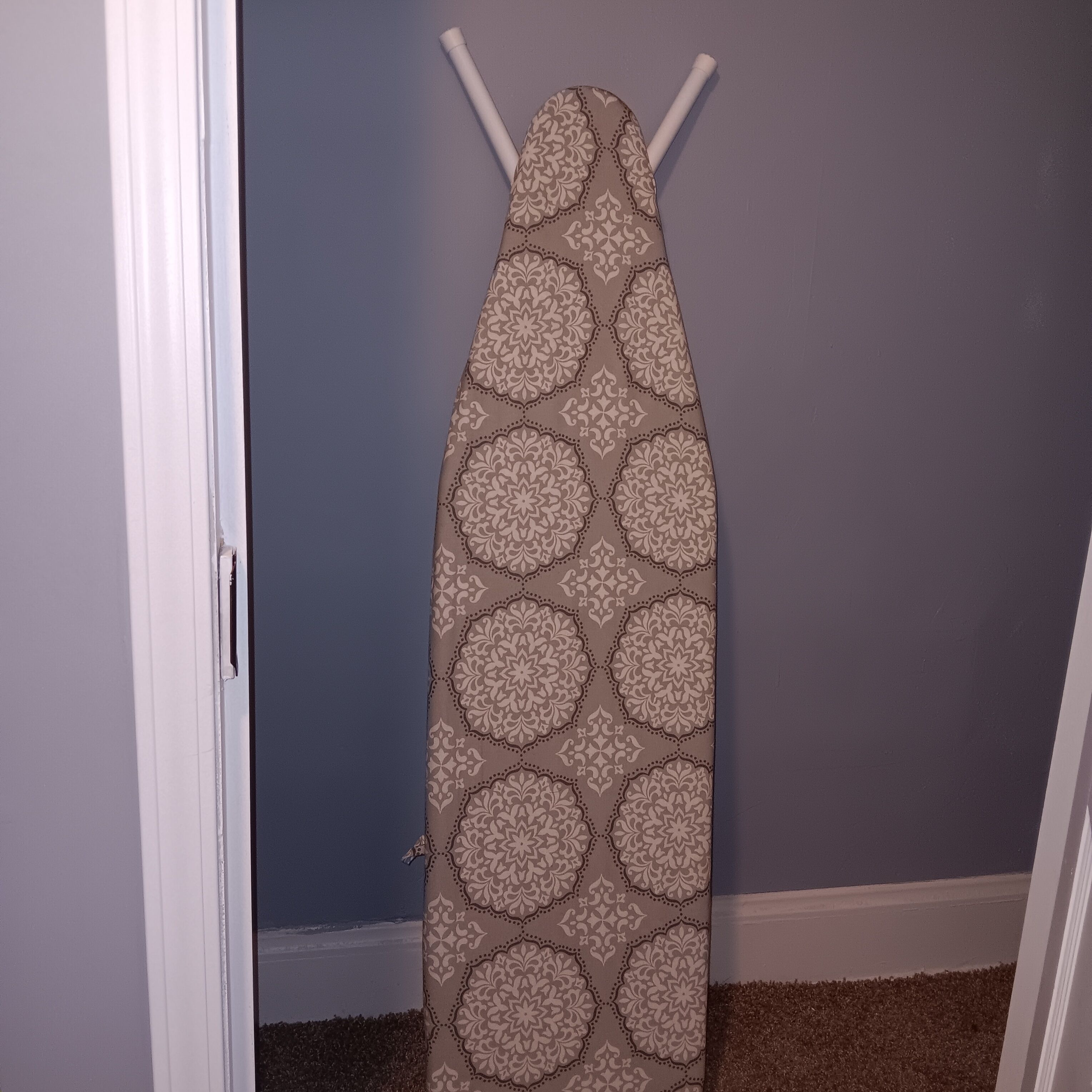 A patterned wall hanging in a room with a door and a carpeted floor.
