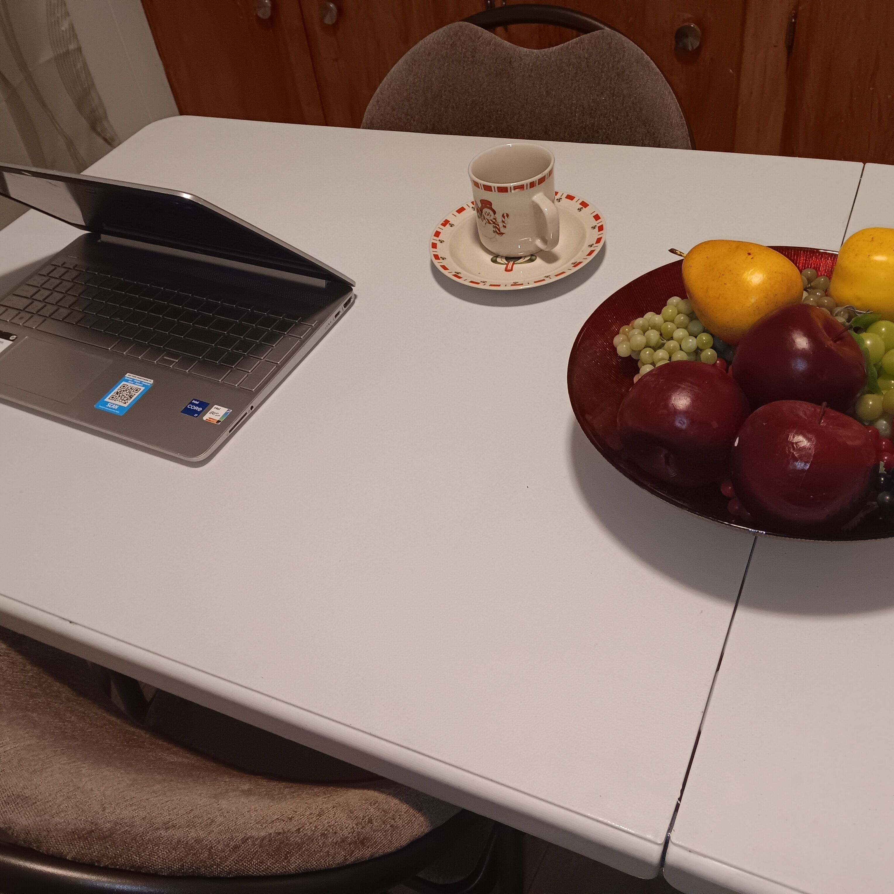 Een laptop op een witte tafel met een schaal fruit en een theetje.
