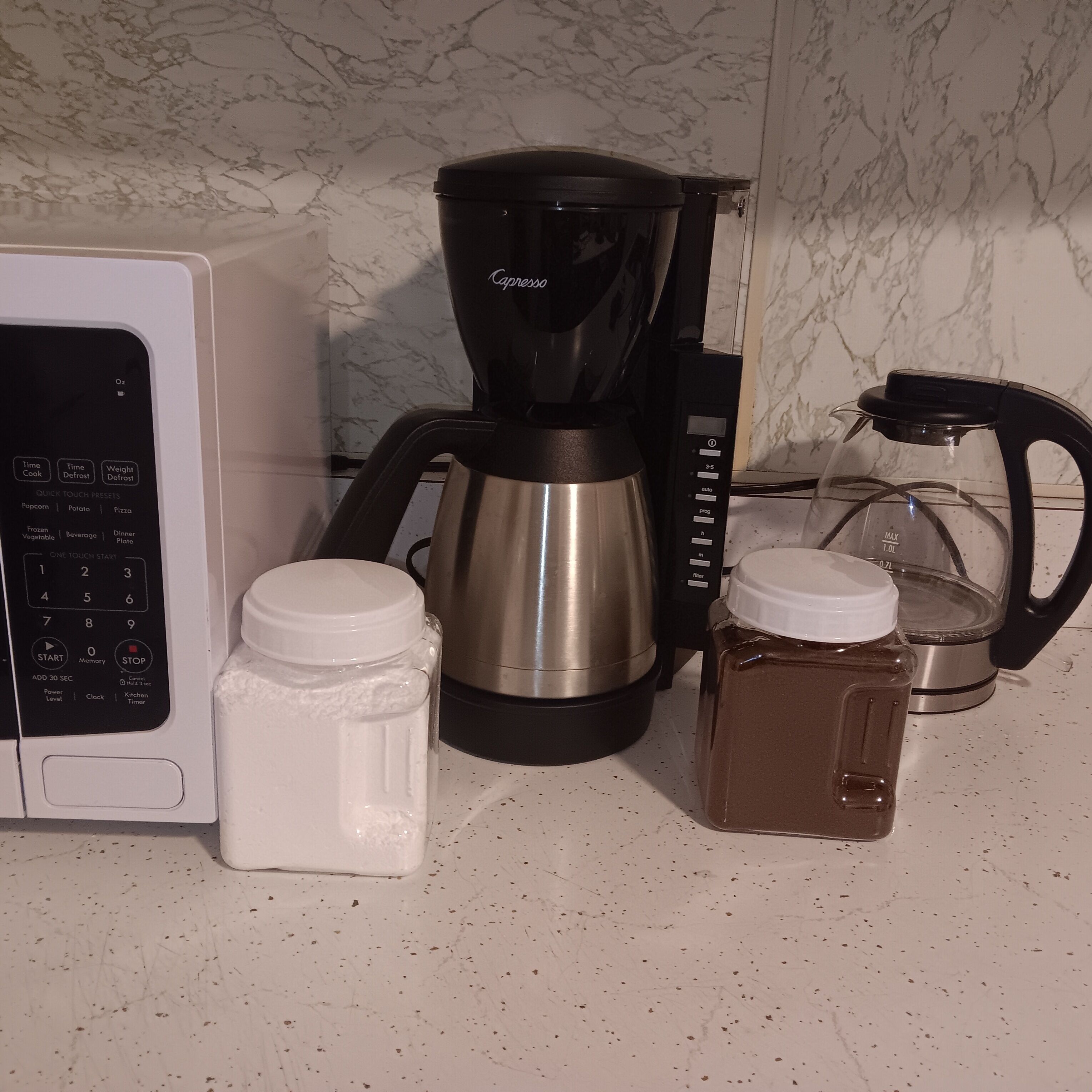 Una encimera de cocina con microondas, cafetera y dos recipientes.