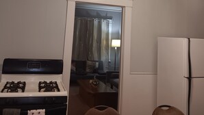 Kompakti keittiö, jossa on kaasuliesi, jääkaappi ja ovi, joka johtaa olohuoneeseen, jossa on sohva ja sohvapöytä.