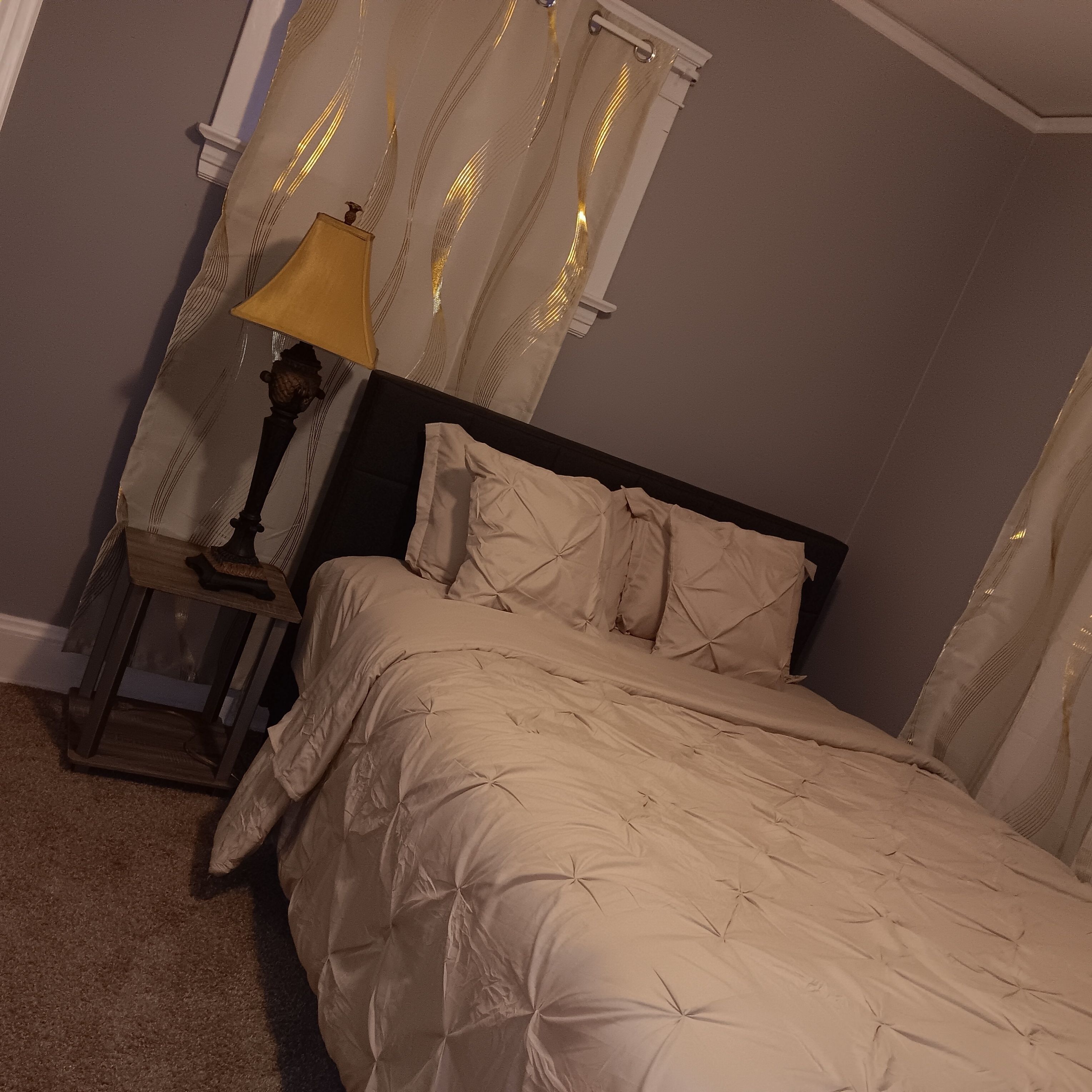 Une chambre à coucher avec un lit, des rideaux, une table de chevet et une lampe.