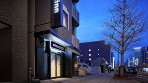 Un edificio moderno con un llamativo letrero 'Minn', una entrada visible y una calle bordeada de árboles.