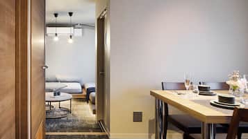 Habitación de hotel con zona de comedor que incluye una mesa de madera para dos personas, un sofá y una mesita redonda con un tapete.