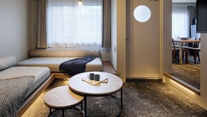 Habitación de hotel con sofá, una mesa redonda con dos tazas, un pequeño tapete y una puerta que da a un comedor.