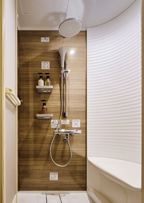 Une douche moderne dotée d’un pommeau de douche à pluie, d’un pommeau de douche à main et d’un appareil de massage à main. Trois étagères accueillent des bouteilles de shampoing et d’après-shampoing.
