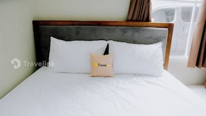 Een net opgemaakt bed met witte beddengoed en een enkel beige kussen met een logo.