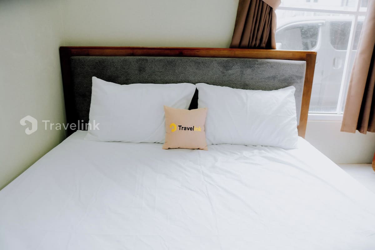 A neatly made bed with white bedding and a single beige pillow with a logo.