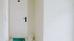 Een witte deur met een klein raam erboven, een deurmat met de tekst 'WELCOME', en een witte mand naast de deur.