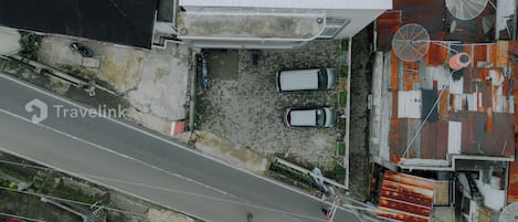 Vue aérienne d’un bâtiment devant lequel sont garées deux voitures, avec une allée pavée et une route qui longe le bâtiment.