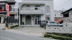 Een modern gebouw met twee verdiepingen, een balkon, een hekwerk en een geparkeerde auto.