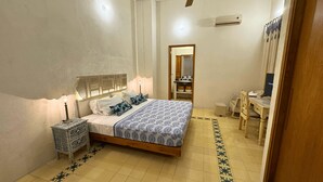 A bedroom with a bed, bedside table, lamp, air conditioning unit, and a small desk with a chair.