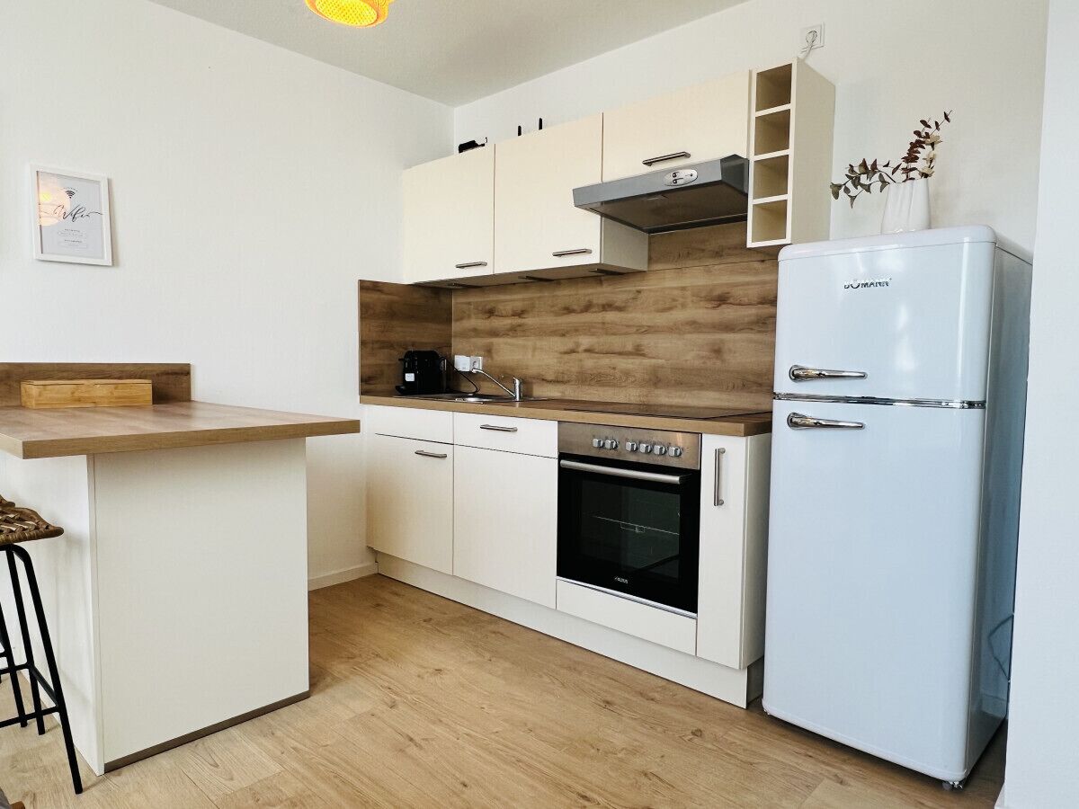 Una cocina compacta con armarios blancos, horno empotrado, refrigerador blanco y encimera de madera.