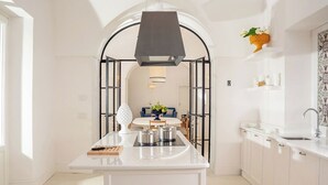 A modern kitchen with a central island, white cabinetry, and a black archway leading to a dining area.