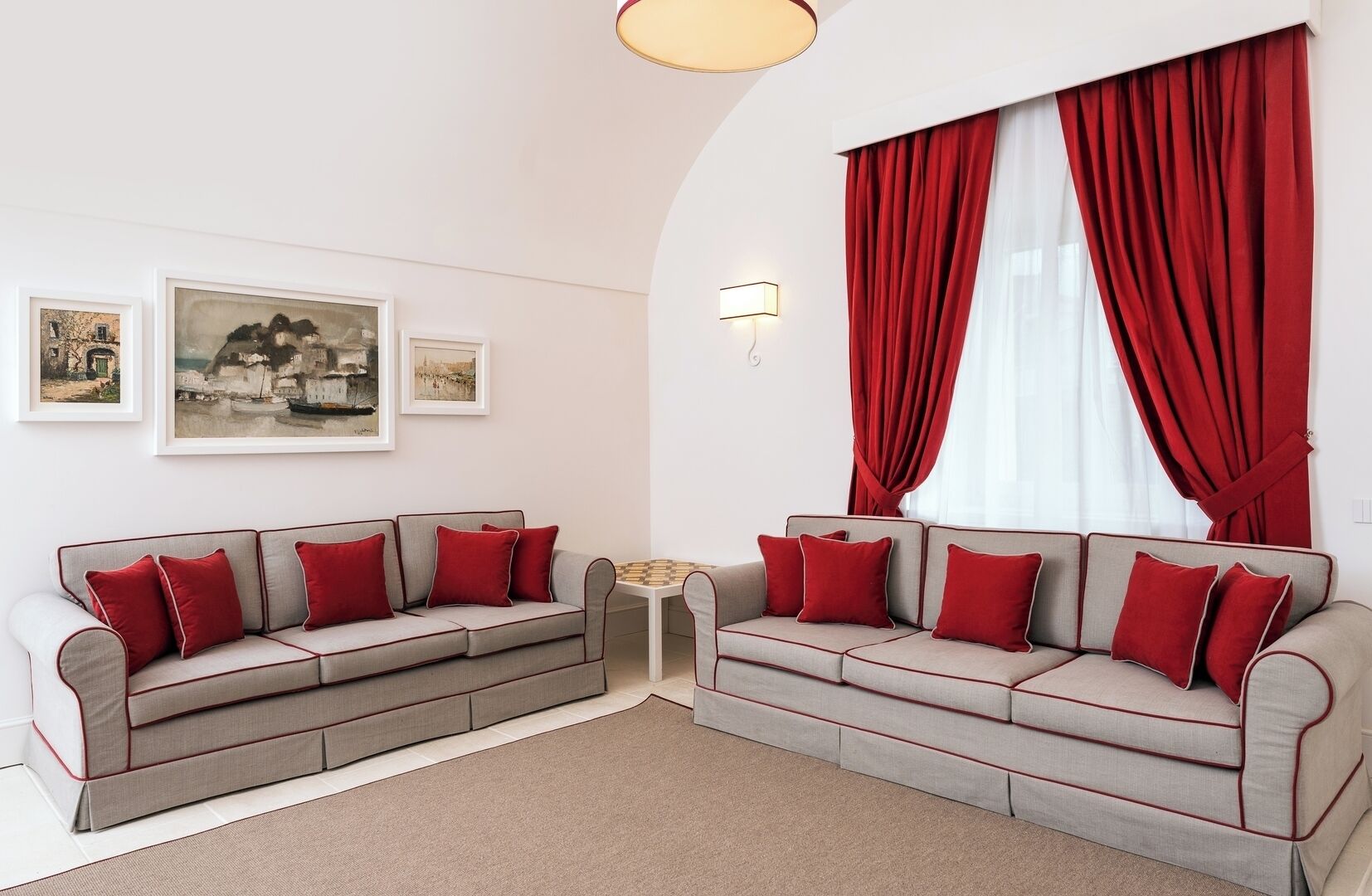 Un salon moderne avec deux canapés gris ornés de coussins rouges, une petite table ronde et des rideaux rouges.