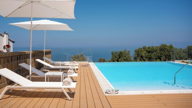 A poolside area with lounge chairs and umbrellas, overlooking a clear blue sky and ocean.