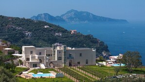 A coastal villa with a swimming pool, garden, and views of the sea and mountains.