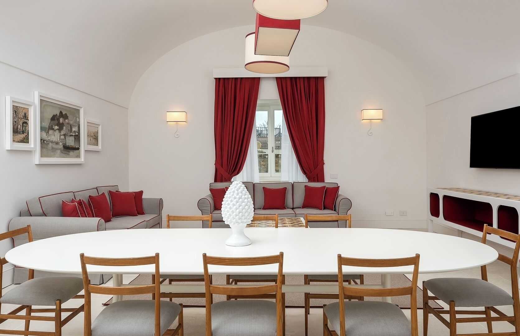 A modern dining room with a round table, wooden chairs, red curtains, and artwork on the walls.