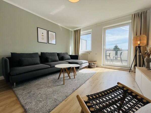 Ein modernes Wohnzimmer mit einem dunkelgrauen Ecksofa, einem runden weißen Couchtisch und Holzböden.