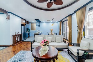 A modern living room with a sofa, a coffee table with a floral centerpiece, a dining area with a chandelier, and a view of the city through large windows. - Luxe Paradise Residence Dang Thai Mai (Hanoi)