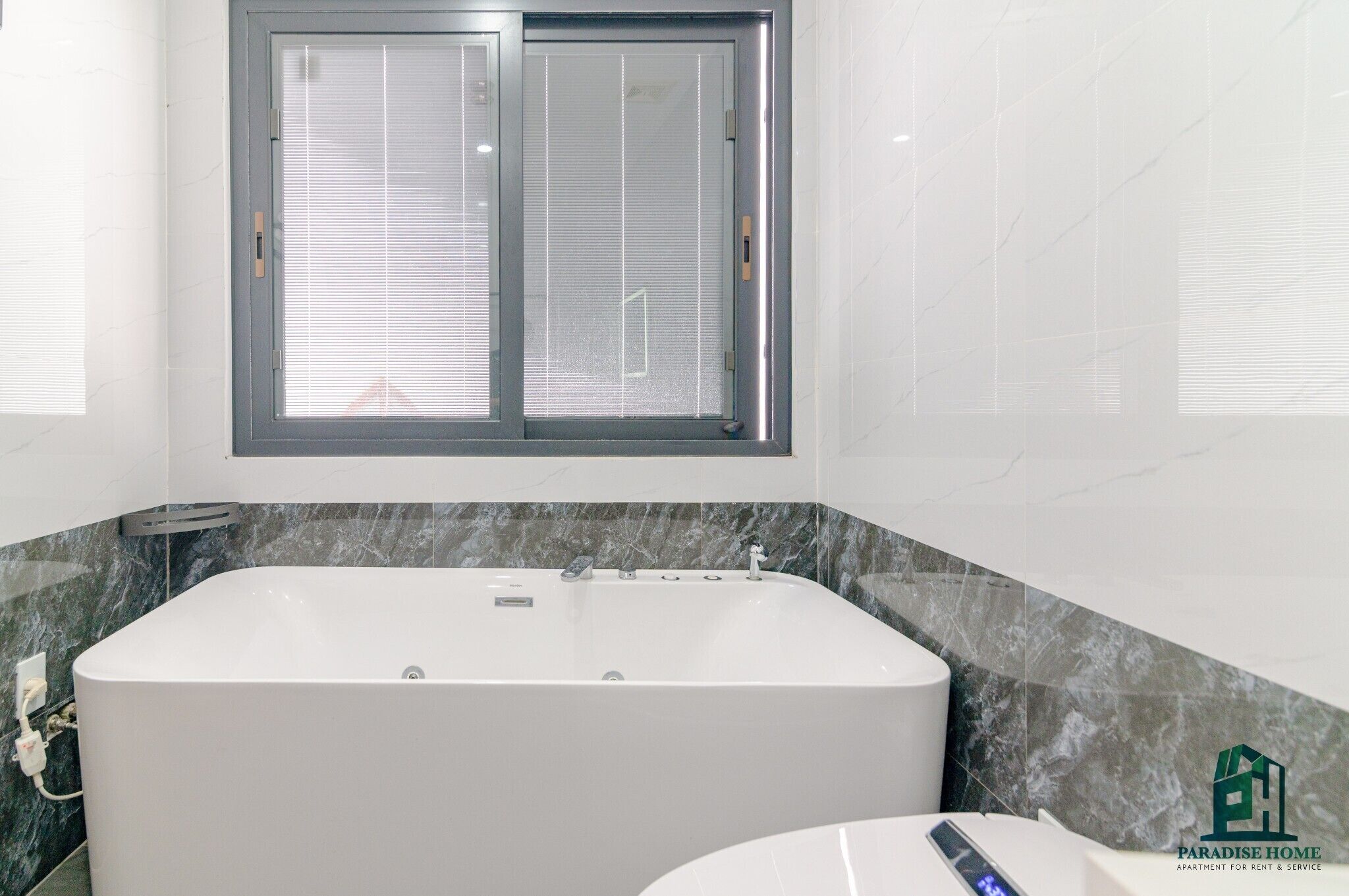 A modern bathroom with a large bathtub, a window with blinds, and a marble countertop.