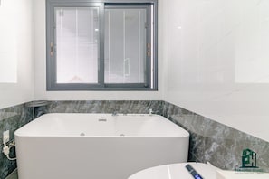 A modern bathroom with a large bathtub, a window with blinds, and a marble countertop. - Luxe Paradise Residence Dang Thai Mai (Hanoi)