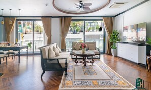 A spacious living room with a sofa, chairs, a coffee table, and a TV. There is a balcony with plants and a view of the outside. - Luxe Paradise Residence Dang Thai Mai (Hanoi)