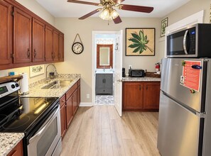 Une cuisine dotée de meubles en bois, d’un réfrigérateur en acier inoxydable, d’un four à micro-ondes, d’une cuisinière et d’un ventilateur de plafond.