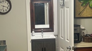 Une salle de bain avec un lavabo blanc, des meubles en bois foncé, un miroir au-dessus du lavabo et une horloge au mur.