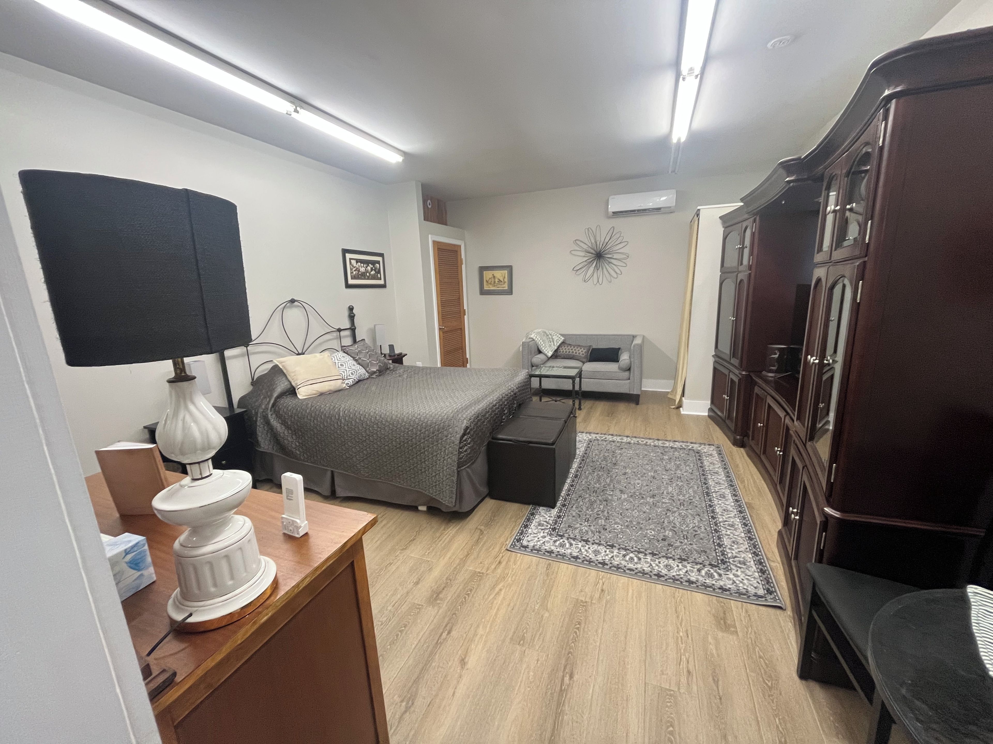 A bedroom with a bed, bedside table, lamp, dresser, and a small rug.