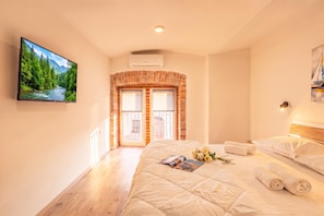 A hotel room with a bed, a TV, a brick fireplace, and a view of a forest.