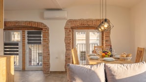 Un comedor con un arco de ladrillo, una mesa dispuesta con platos, vasos y una cesta de fruta.