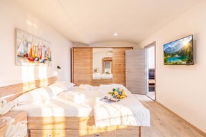 A modern hotel room with a bed, a painting of sailboats, a television, and a view of a mountain lake. - Rijeka City Vibes Apartment, Rijeka, Croatia (Rijeka)