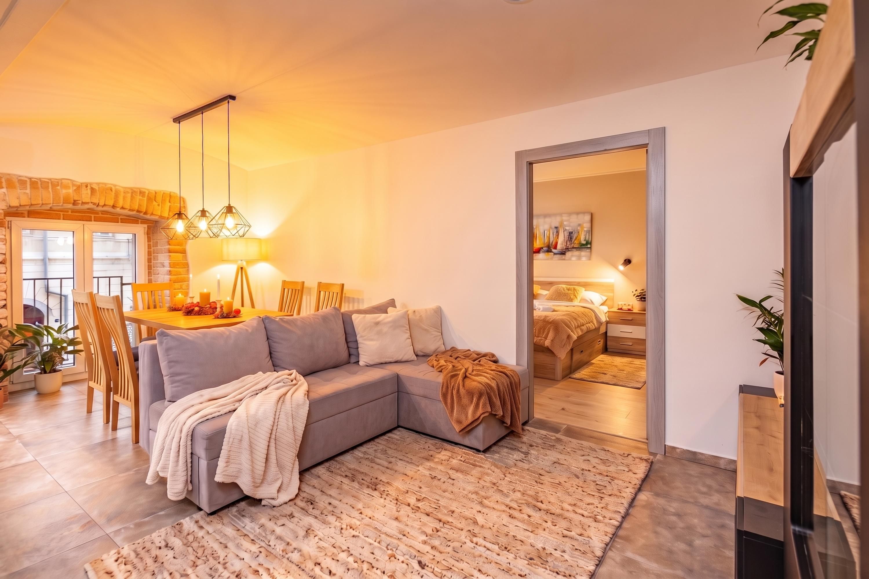 Una sala moderna con un sofá seccional, un comedor con chimenea de ladrillo y un dormitorio con cama y mesita de noche.