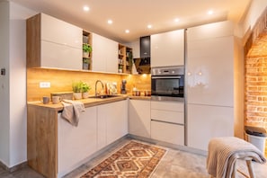 A modern kitchen with a wooden countertop, built-in cabinets, a stainless steel oven, and a brick accent wall.