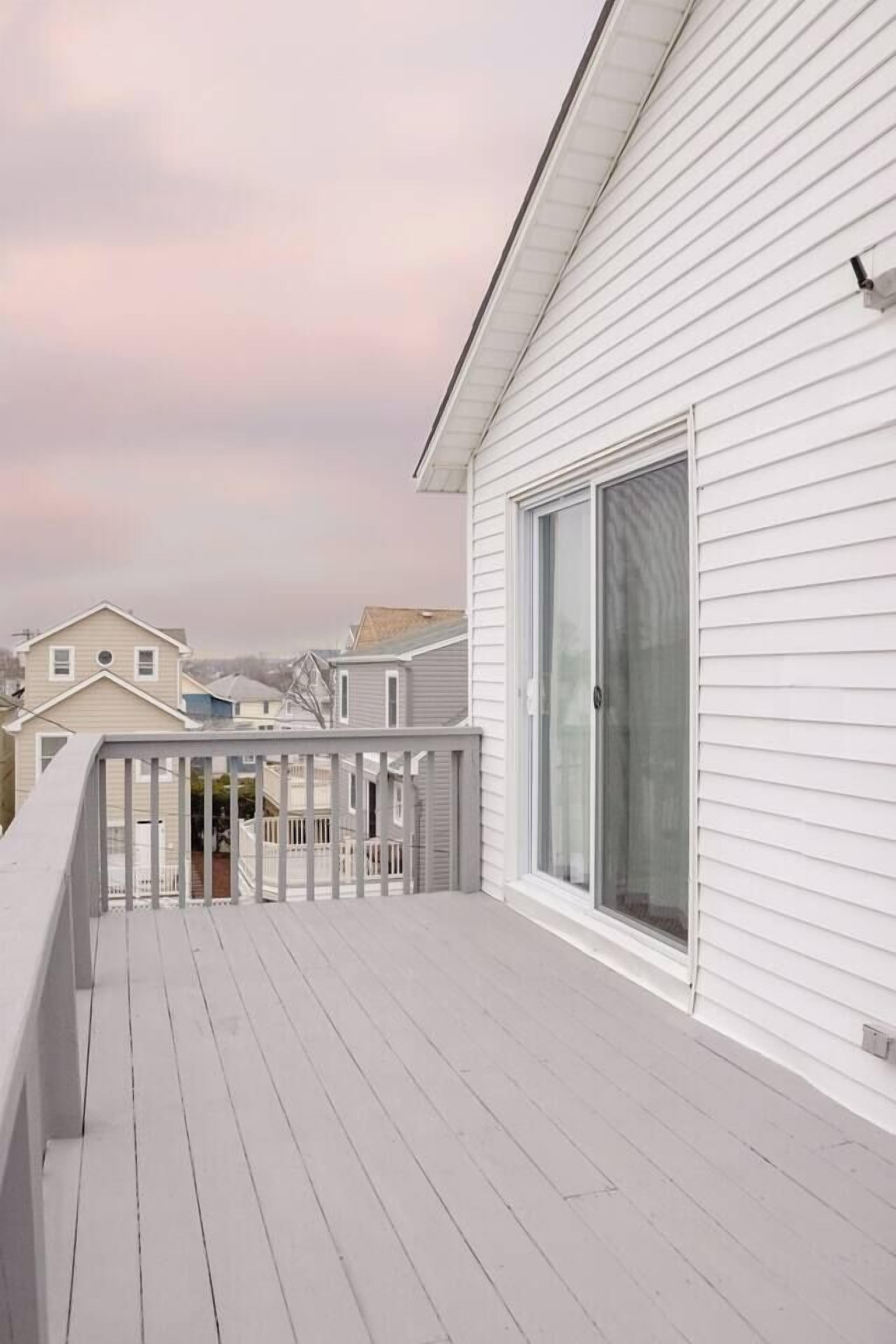 Eine weiße Holzdielen-Terrasse mit einer Glastür, die zu einem Balkon führt.