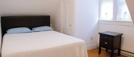 A bedroom with a bed, a nightstand, a door, and a window.