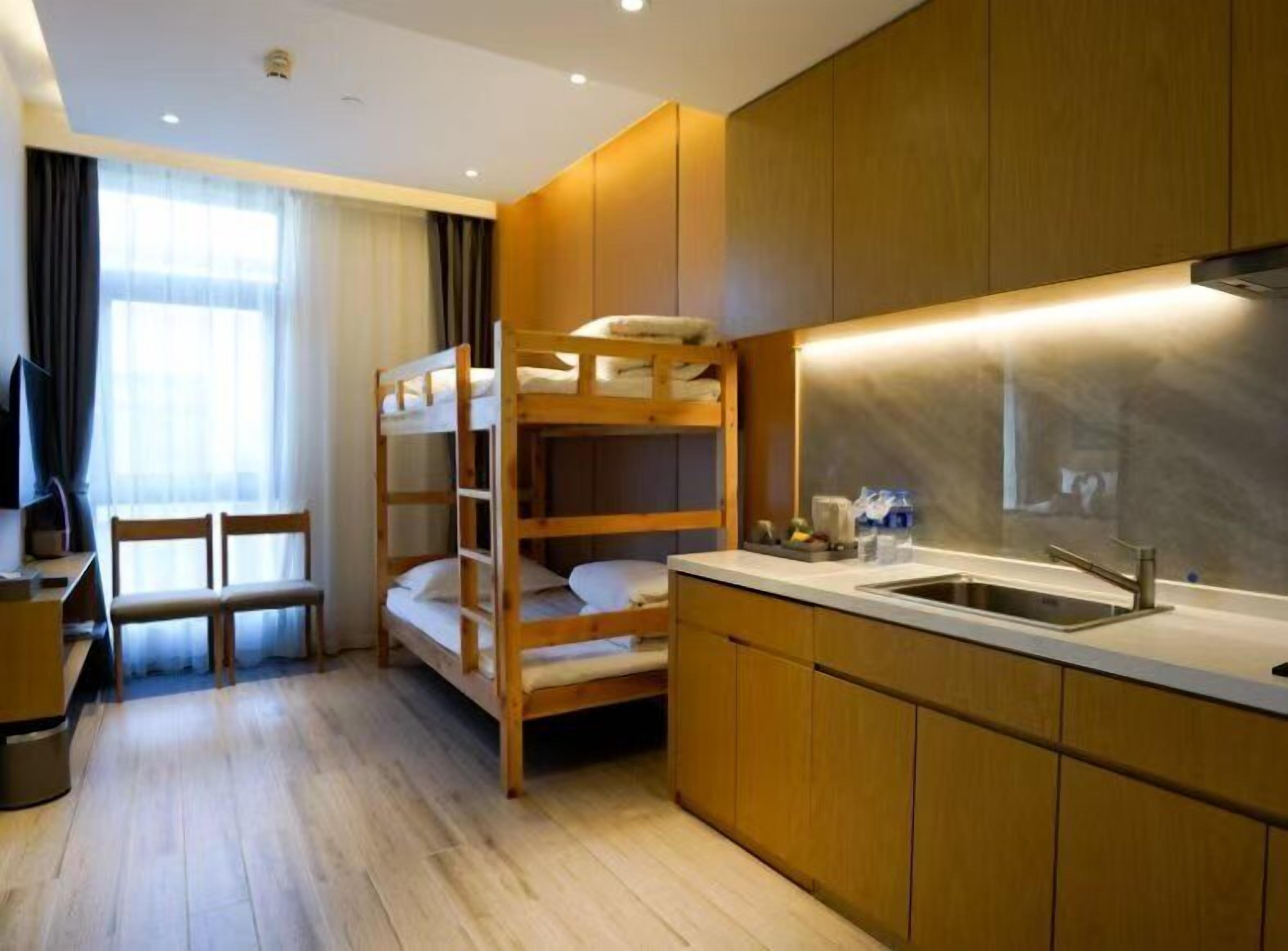 Une chambre d’hôtel compacte avec des lits superposés, une petite kitchenette, un coin repas et une grande fenêtre avec des rideaux.