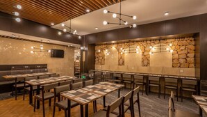 A restaurant with multiple tables and booths, a stone wall feature, and modern lighting fixtures.