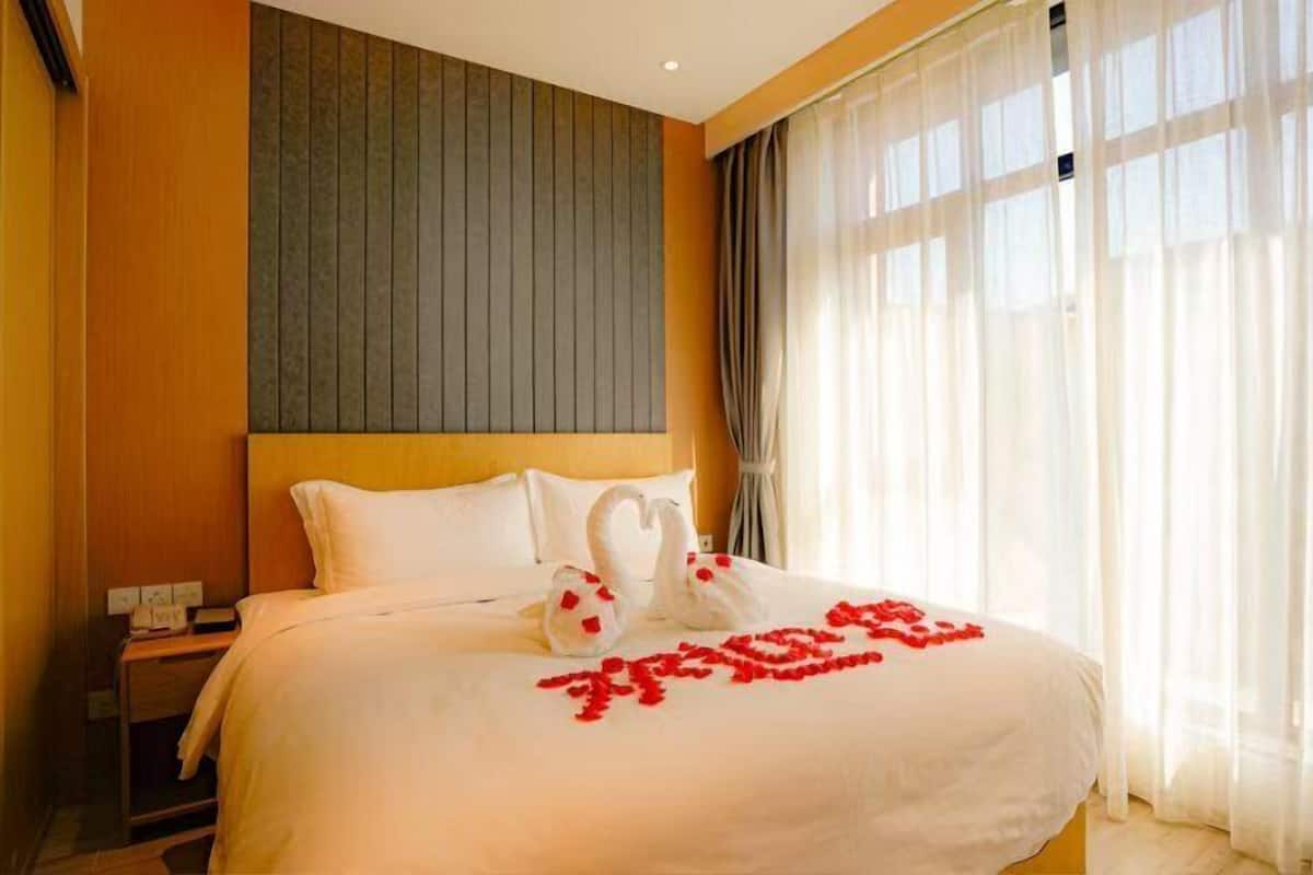 Ein Hotelzimmer mit Bett, Nachttisch und Fenster mit leichtem Vorhang.