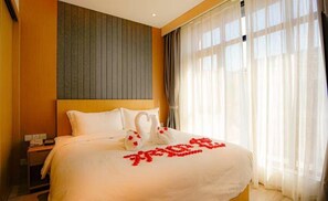 Ein Hotelzimmer mit Bett, Nachttisch und Fenster mit leichtem Vorhang.