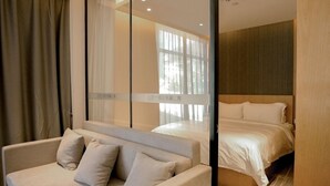 A modern hotel room with a bed, a sofa, and a large window with sheer curtains.