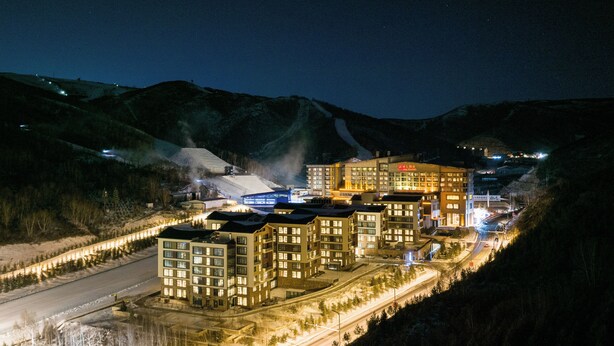 A hotel with multiple buildings, a ski lift, and a snow-covered landscape at night.