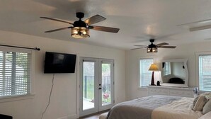 Un dormitorio con una cama, ventiladores de techo, un televisor y una ventana.