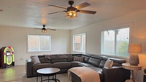 Una sala de estar con un sofá modular, una mesa de centro redonda, un ventilador de techo y un jukebox.