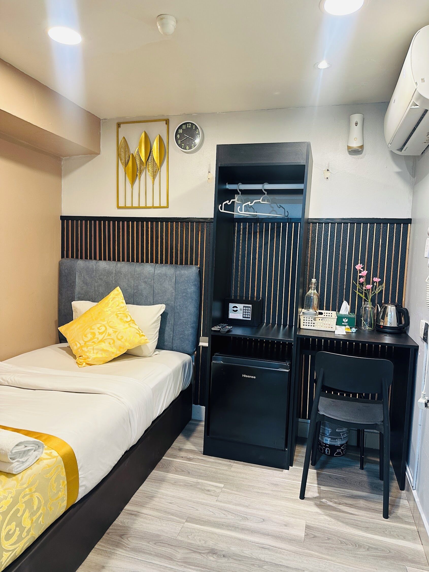 A hotel room with a bed, a desk, a chair, a small fridge, a heater, and a wall-mounted air conditioner.